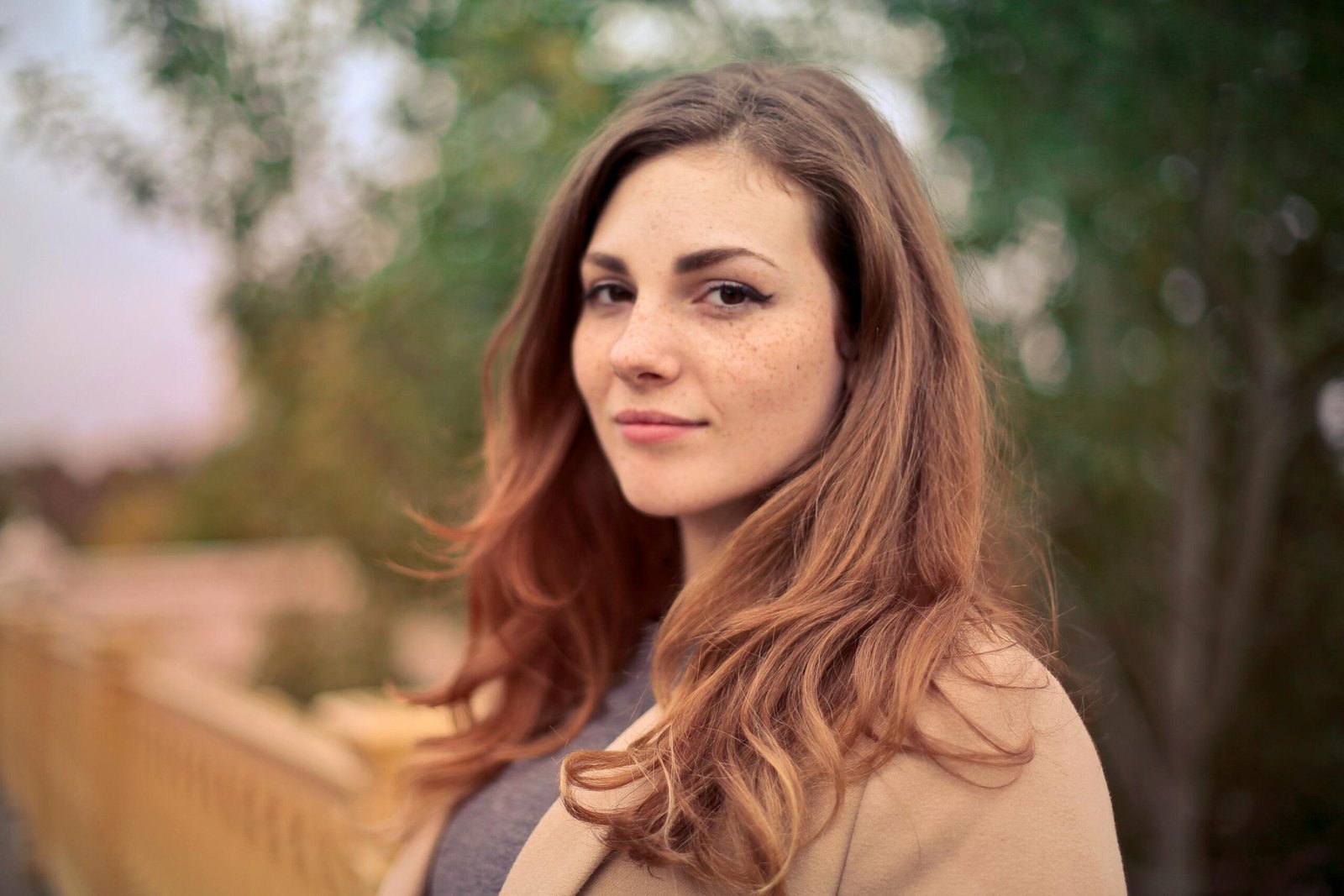 Home A young woman with long hair smiles confidently for an outdoor portrait session.
